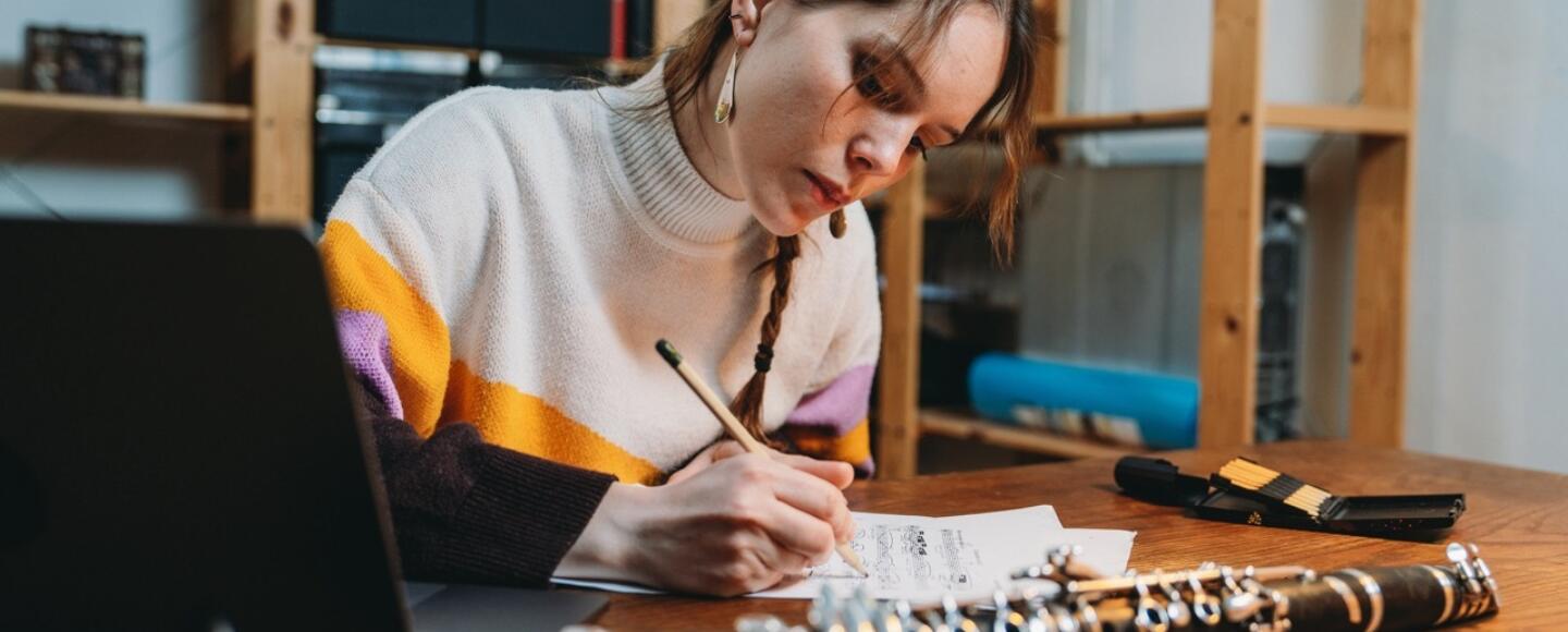 A musician sits writing music with a clarinet in front of her