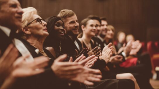 The audience in the front row of a concert smiles and applauds